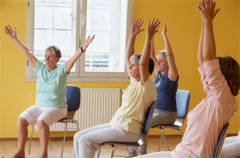 Stock photo of three seniors seated in chairs with their hands in the air
