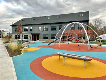 Photo of the Golden Hill Apartment Complex, with a colorful playground in the foreground and two story blue gray building in background.