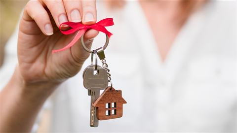 Close up photo of hand holding a key with a keychain shaped like a house